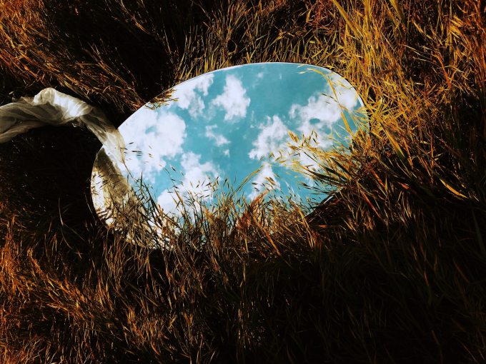 Oval mirror sits on browning grass and reflects clouds in the sky